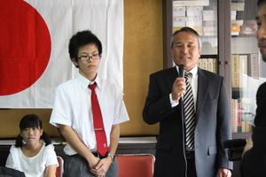 男子生徒の隣で校長先生が挨拶をしている写真