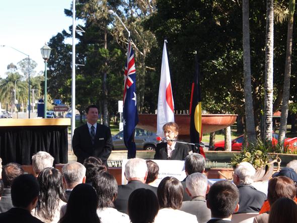 オーストラリアと日本の国旗が飾られたセレモニーで挨拶をしている人の写真