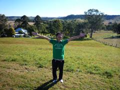 緑のTシャツをきた男性が草原の中で大きく手を広げている写真