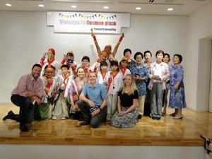 市民交流センターでお揃いの衣装を着た人たちと関係者の人達、4名の外国人の方が記念撮影をしている写真