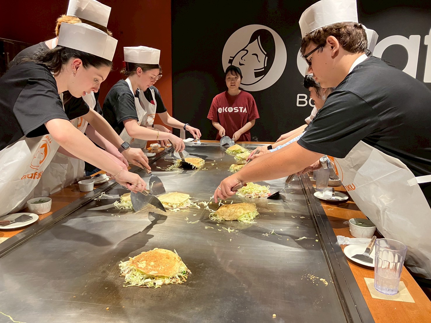 リズモー市の派遣学生4名と、引率教師1名が、夕食のため、鉄板お好み焼き体験のできる店に行き、店員に焼き方を教えてもらい、自分たちでお好み焼きを作って食べました。