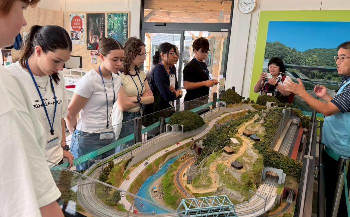 8人の者が地すべりのジオラマに囲まれ見ている様子