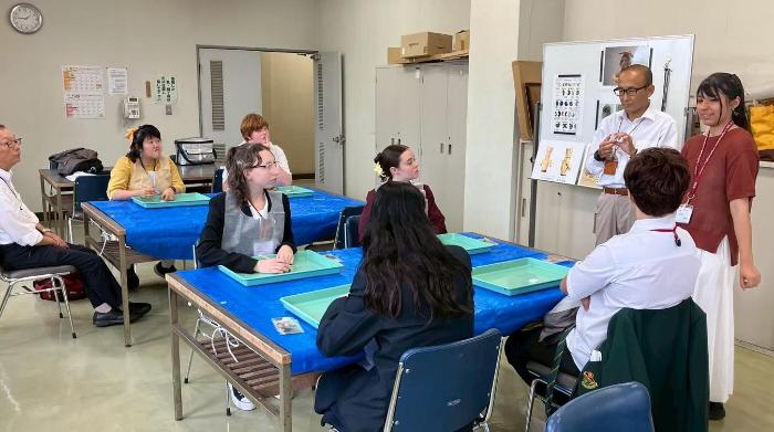 テーブルで7人の者に向けて1人の男性と1人の女性が勾玉の説明をしている様子