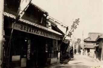 右から文字がかかれた看板がある昔のお店の入り口を写した白黒写真