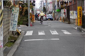 道路両脇に電信柱が立ち自転車で走行している人の後ろ姿を写した写真