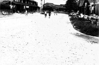 砂利道を着物姿の女性が歩いている後ろ姿を写した白黒写真