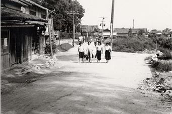 本町商店街の道路を女性が4名が横並びで歩いている昔の白黒写真