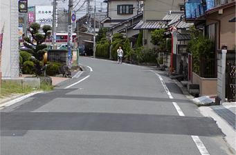 民家が立ち並ぶ緩やかなカーブの道路を1人の男性が歩いている写真