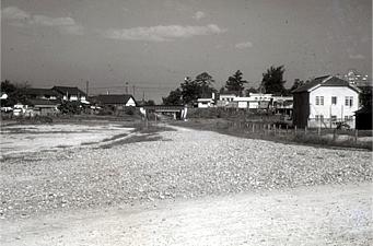 手前の石がたくさんある道の奥に数件建物がある昔の高田市駅南側の白黒写真