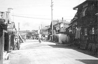 舗装前の道路を自転車で通行している人を写した昔の天神橋商店街近くの白黒写真