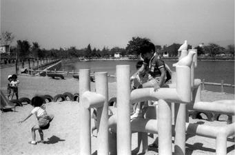 大中公園の池の横にある遊具で元気に遊んでいる子供たちの白黒写真