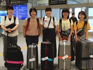 大きなスーツケースを持ち空港で並んでいる女子学生5名の写真