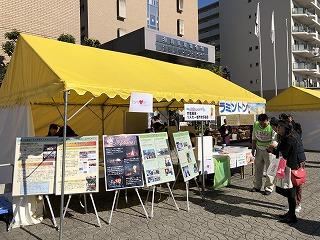 黄色の屋根のテントでラミントン販売と5枚の案内板を店先に並べている出店様子の写真