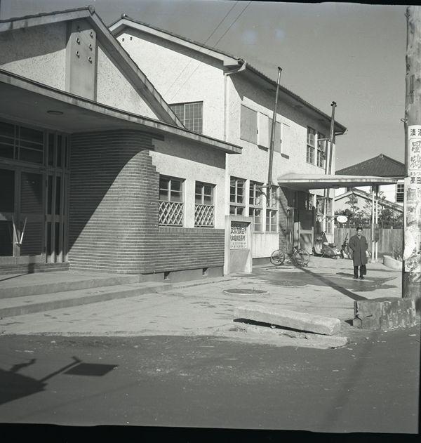 白い外壁をした昔の県中和労働会館の建物を斜めから写し、その前に1人の男性がだっている白黒写真