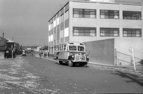 真四角の電話公社建物の横の道路を走るボンネットバスの白黒写真
