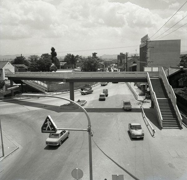 片塩ロータリーの横断歩道橋と車線がかかれていない道路を走る車を上空から写した白黒写真