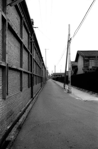 道路沿いに建つ建物の赤レンガ造りの壁を写した白黒写真