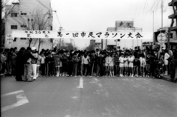 市制30周年第1回市民マラソン大会の幕の下でたくさんの参加者の人達がスタートを待っている白黒写真