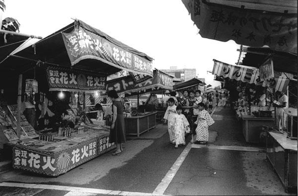 浴衣をきた家族連れの人達が夏祭りの出店を楽しんでいる白黒写真