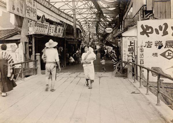 天神橋を赤ちゃんを抱き歩いている女性の奥には商店街が見える白黒写真