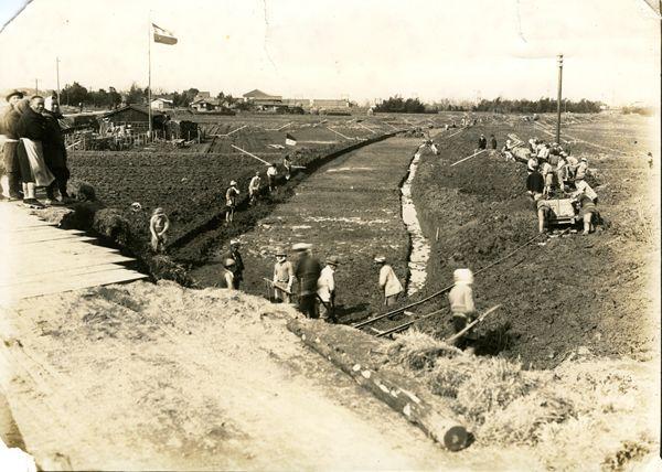 作業員の人達が田んぼを川にする工事をしている白黒写真