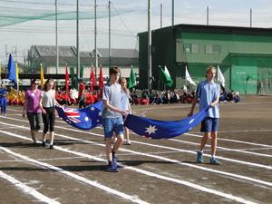 2組の男女それぞれがオーストラリアの国旗を持ち、体育祭の入場をしているリズモー市の学生5名の写真