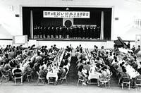 舞台の上で合唱をしている人と鑑賞している人達を写した白黒写真