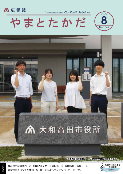 広報誌8月号表紙 「大和高田市役所」と書かれた市役所正面玄関前の石碑のうしろでガッツポーズをする令和4年に採用された新規職員4人