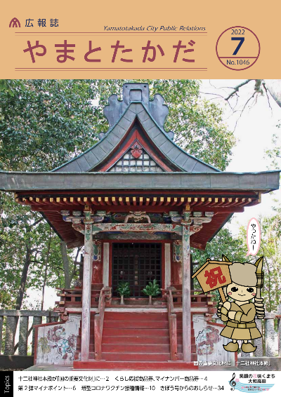 広報誌7月号表紙 「祝」と書かれた看板を持った大和高田市生涯学習課文化財係のマスコットキャラクター「ゆぎ丸」と、国の指定重要文化財になった「十二社神社本殿」の写真