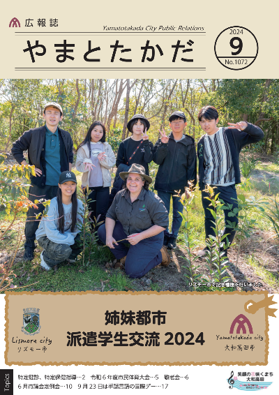 広報誌9月号表紙 大和高田市との姉妹都市であるオーストラリアのリズモー市に派遣された5人の学生が植樹を行なった森林で撮影した記念写真。中央には現地のガイドさんが写っており、その周りを5人の学生と引率した先生が囲んでいる。