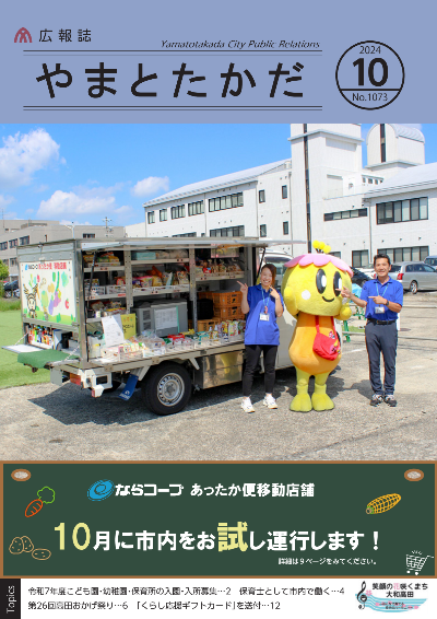令和6年10月に市内を試行運転するならコープのあったか便移動店舗の前で、従業員さん2人と大和高田市のマスコットキャラクターみくちゃんが車を指差すポーズをとっている写真。背景は芝生。